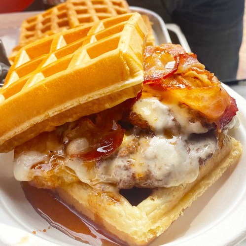 A delicious burger with melted cheese and bacon, sandwiched between two waffles, drizzled with syrup.