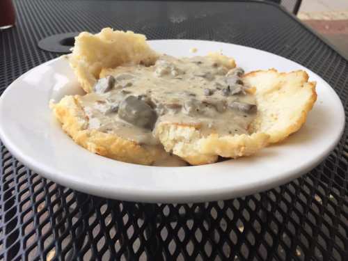 A plate of biscuits topped with creamy sausage gravy, served on a black metal table.
