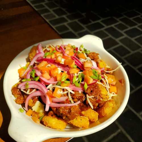 A bowl of spicy mixed snacks topped with chopped onions, tomatoes, and green herbs.
