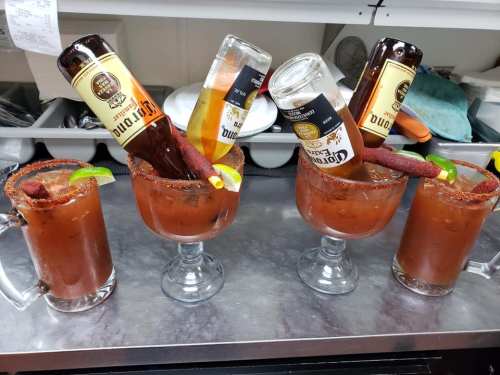 Four large glasses of Bloody Marys with beer bottles upside down, garnished with lime and a spicy rim.