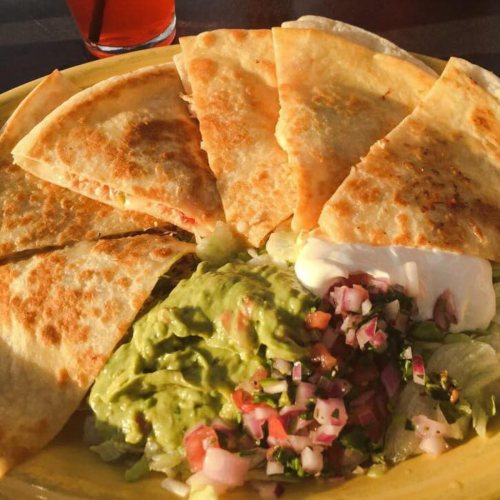 A plate of quesadillas with guacamole, pico de gallo, and sour cream on the side, served in warm sunlight.