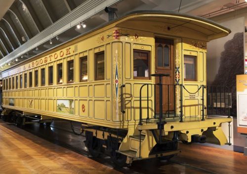 A vintage yellow train car displayed in a museum, featuring ornate decorations and wooden doors.