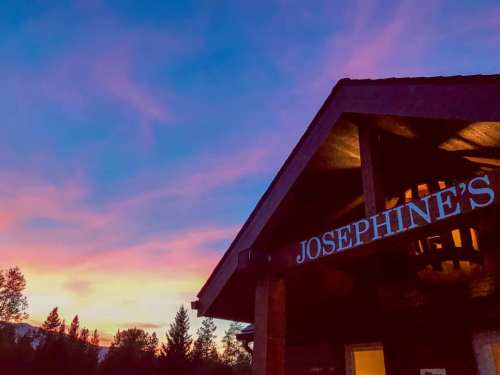 A wooden building with a sign reading "Josephine's" against a vibrant sunset sky filled with pink and purple hues.
