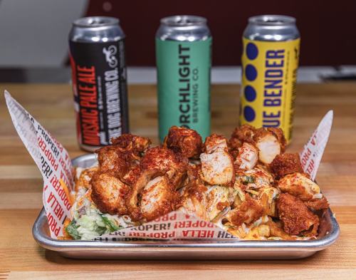 A tray of spicy chicken bites on a bed of lettuce, with three colorful beer cans in the background.