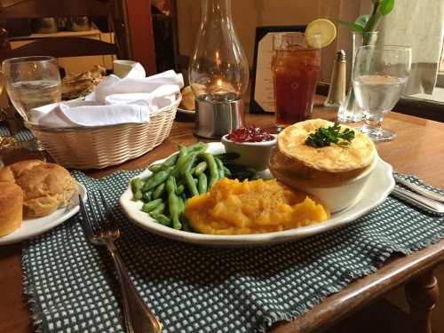 A plate with green beans, mashed squash, and a biscuit, set on a wooden table with drinks and a basket of bread.