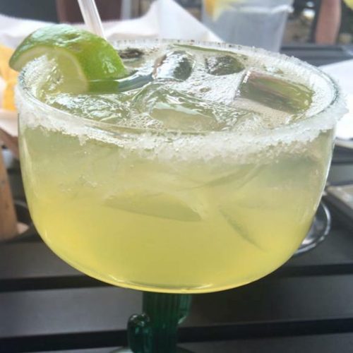A refreshing green cocktail with a lime wedge and salt rim, served in a large glass on a table.