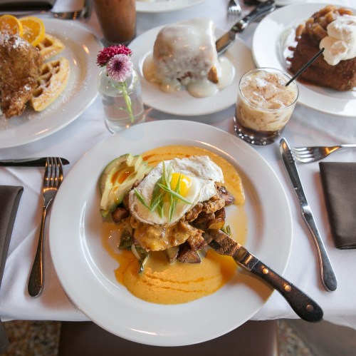 A plate of breakfast featuring a fried egg on avocado and potatoes, surrounded by various brunch dishes and drinks.