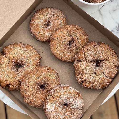 A box of freshly baked, cinnamon-sugar coated donuts arranged neatly inside.