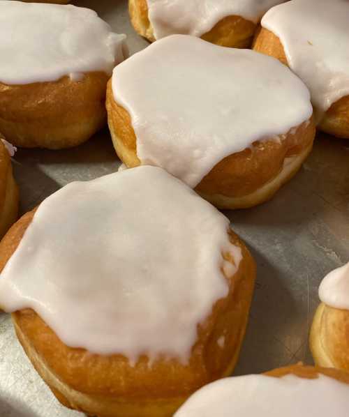 A close-up of freshly baked donuts with a glossy white icing on top, arranged on a baking tray.