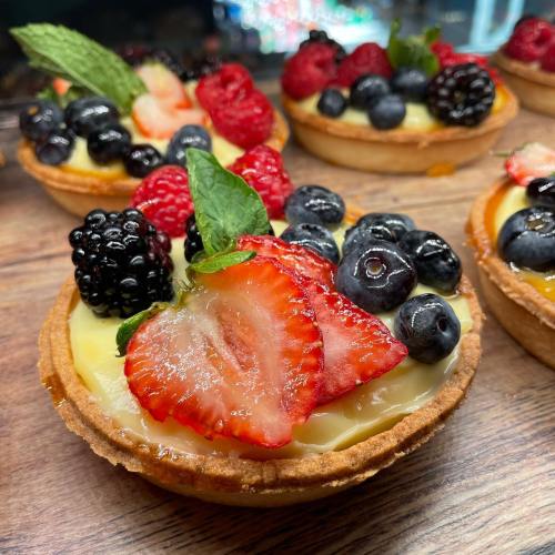 Colorful fruit tarts topped with strawberries, blueberries, raspberries, and blackberries on a wooden surface.