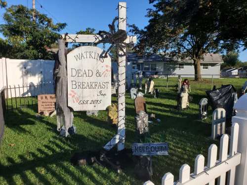 A spooky yard display featuring a sign for "Watkins Dead & Breakfast" with tombstones and Halloween decorations.