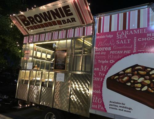 A brightly lit food truck named "The Brownie Bar," featuring a menu of various brownie flavors and desserts.