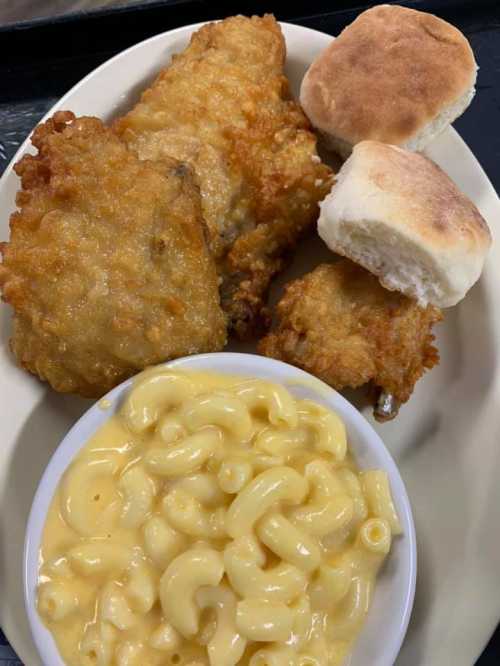 A plate featuring fried chicken, two biscuits, and a bowl of creamy macaroni and cheese.