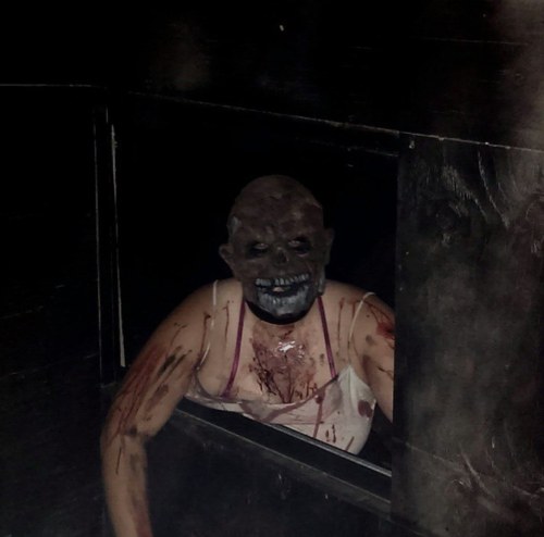 A creepy figure with a skull mask and blood-stained clothing emerges from a dark space, creating a horror atmosphere.