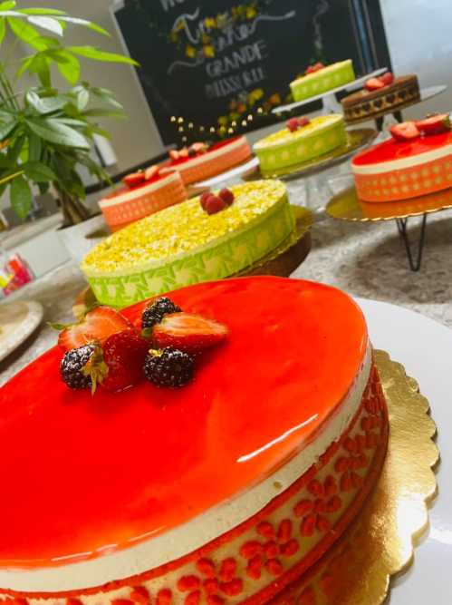 A variety of colorful cakes topped with fresh strawberries and blackberries, displayed on a table.