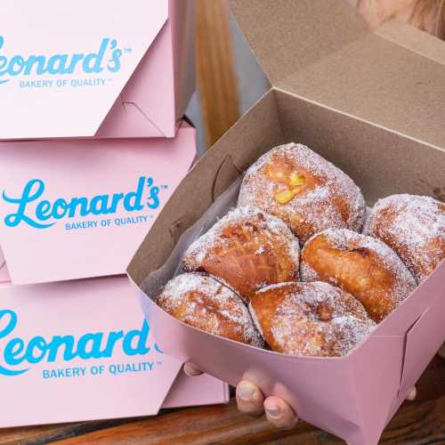 A box of freshly baked pastries dusted with sugar, placed on a wooden surface with branded packaging in the background.