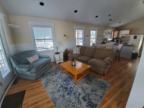 Cozy living room with a blue couch, beige sofa, wooden coffee table, and kitchen in the background. Bright and inviting space.