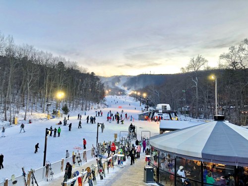 A snowy ski resort scene with skiers on the slopes, surrounded by trees and illuminated by evening lights.