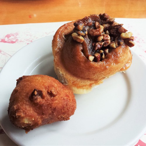 A plate with a cinnamon roll topped with nuts and a small round pastry beside it.