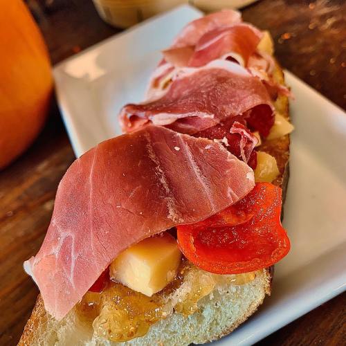 A close-up of a sandwich topped with cured meats, cheese, and sliced peppers on a toasted bread slice.