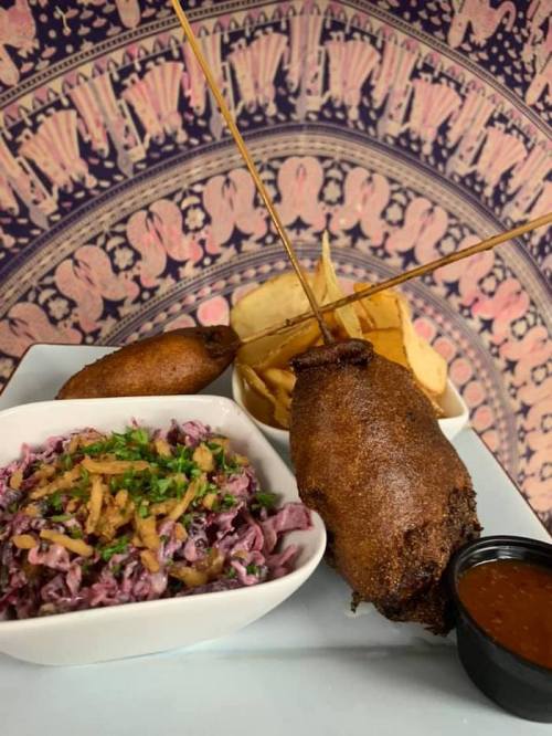 A plate featuring two fried items on skewers, a side of purple cabbage slaw, and dipping sauce, with a decorative background.