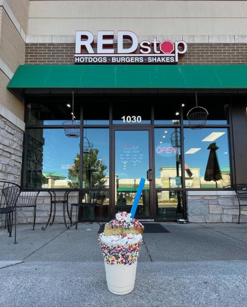 A colorful ice cream sundae with sprinkles sits in front of REDstop, a restaurant featuring hot dogs, burgers, and shakes.