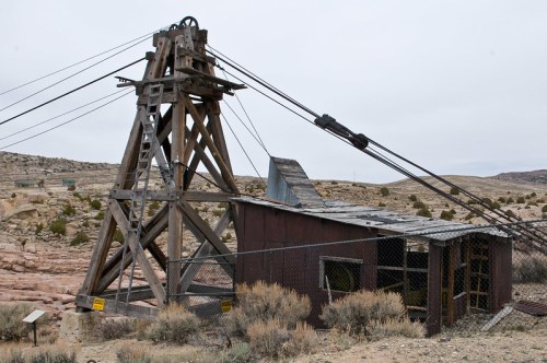 An old mining structure with a wooden frame and cable system, surrounded by barren landscape and sparse vegetation.