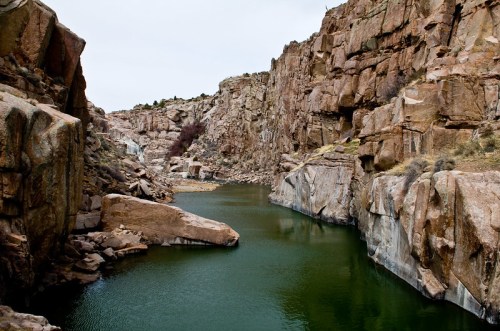 A serene river flows between steep, rocky cliffs under a cloudy sky.