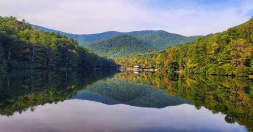 A serene lake surrounded by lush green trees and mountains, reflecting the landscape in calm waters.