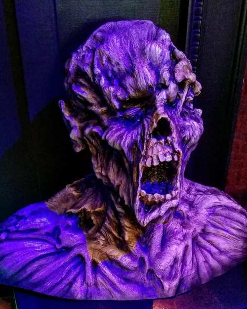 A detailed, purple-hued sculpture of a monstrous face with an open mouth, showcasing intricate textures and features.