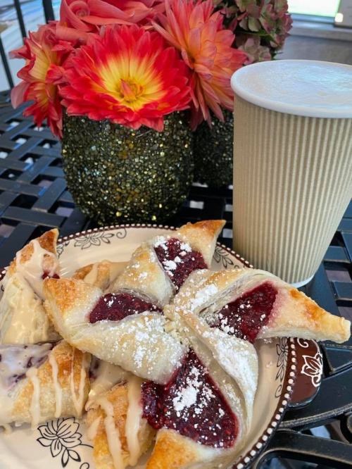 A plate of pastries with fruit filling, powdered sugar, and a coffee cup, alongside vibrant flowers in decorative vases.