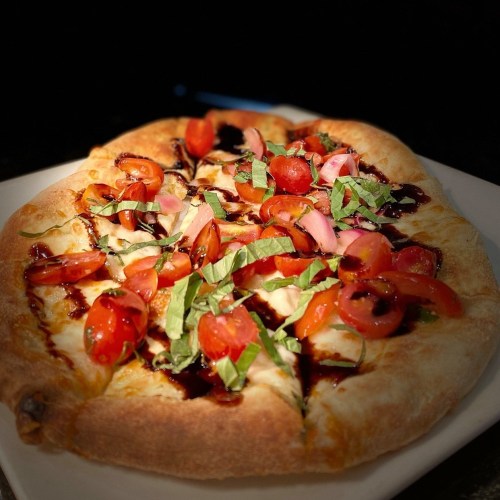 A freshly baked pizza topped with cherry tomatoes, basil, and a drizzle of balsamic glaze on a white plate.