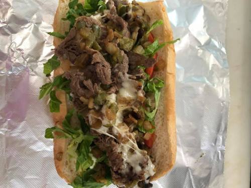 A loaded sandwich with sliced beef, lettuce, tomatoes, and green peppers on a hoagie roll, wrapped in foil.