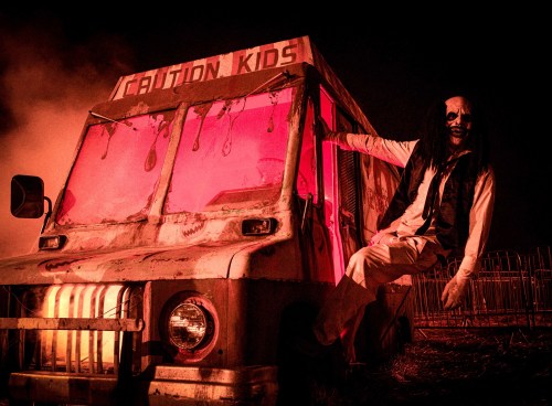 A creepy, abandoned food truck with a sinister figure hanging out, illuminated by eerie red light in a dark setting.