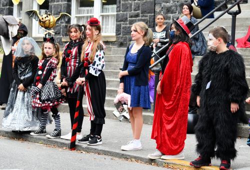 A group of children in various costumes, including a clown, witch, and monster, lined up for a Halloween event.