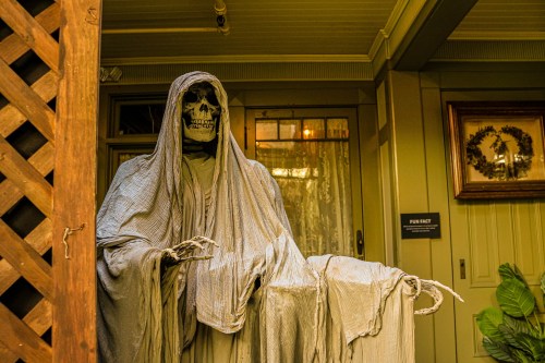 A skeletal figure draped in gray fabric stands at a doorway, creating a spooky Halloween atmosphere.
