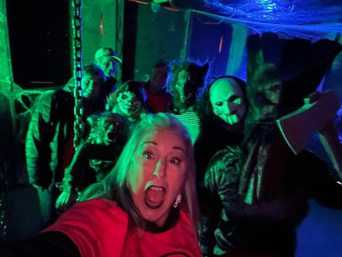 A group of people in Halloween costumes pose for a selfie in a spooky, dimly lit setting with green lighting.