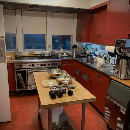 A modern kitchen with red cabinets, stainless steel appliances, and a wooden table with bowls and jars on it.