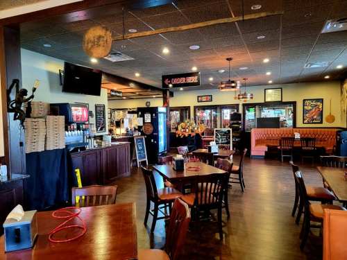 Interior of a restaurant featuring wooden tables, chairs, a bar area, and a cozy atmosphere with warm lighting.