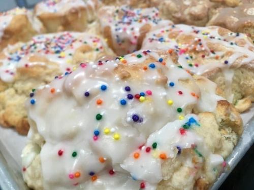 Close-up of freshly baked biscuits topped with white icing and colorful sprinkles.