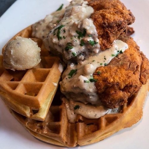 A plate featuring crispy fried chicken on a waffle, topped with creamy gravy and a scoop of butter.