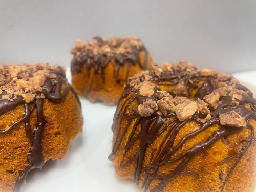 Three mini bundt cakes topped with chocolate drizzle and crushed nuts, set against a light background.