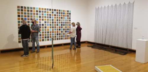 Visitors explore an art gallery featuring a colorful grid of artworks and various sculptures in a spacious room.
