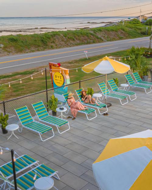 Two people relax on lounge chairs by the beach, with colorful umbrellas and a scenic view of the ocean in the background.