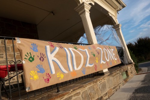A large banner reading "KIDZ ZONE" with colorful handprints, displayed on a porch railing.
