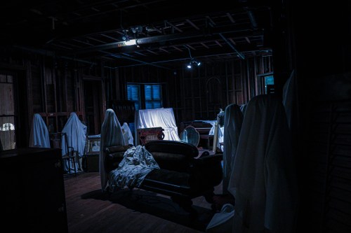 A dimly lit room with covered furniture and ghostly figures draped in white sheets, creating an eerie atmosphere.