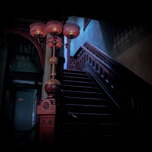 A dimly lit staircase with ornate wooden railings and a vintage lamp casting a warm glow.