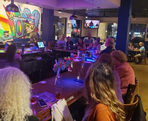 A lively bar scene with patrons enjoying music and entertainment, colorful artwork on the wall, and a cozy atmosphere.