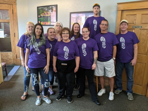 A group of 12 people wearing purple t-shirts with a footprint design, smiling together in a restaurant setting.