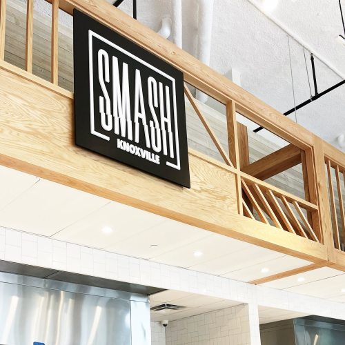 Sign reading "SMASH KNOXVILLE" displayed on a wooden wall in a modern interior space.